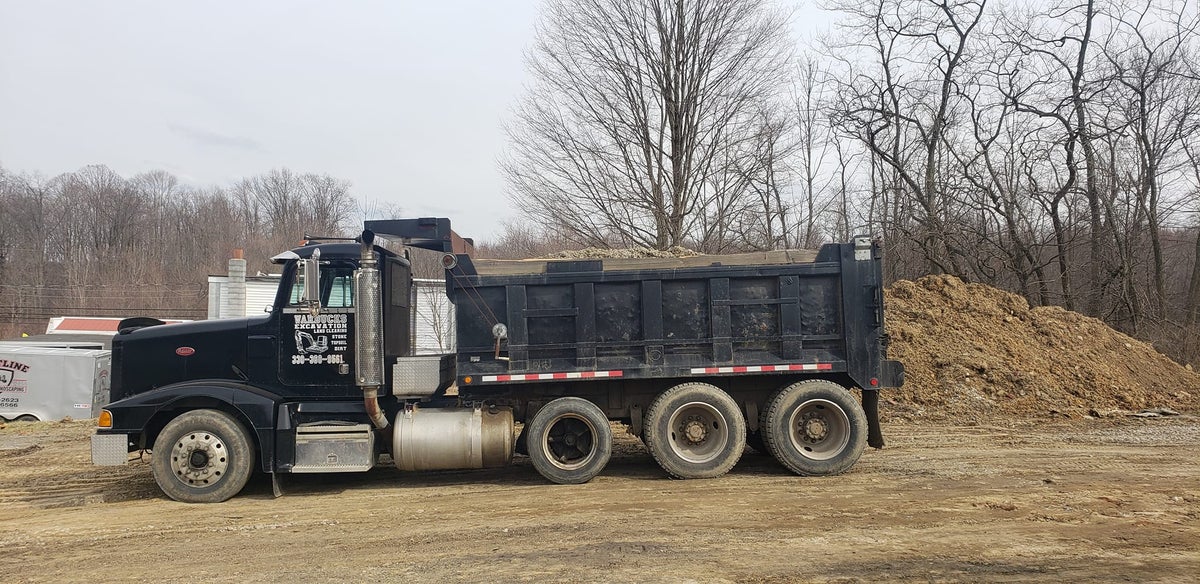 Warbucks dump truck staged beside a material pile for hauling and delivery work